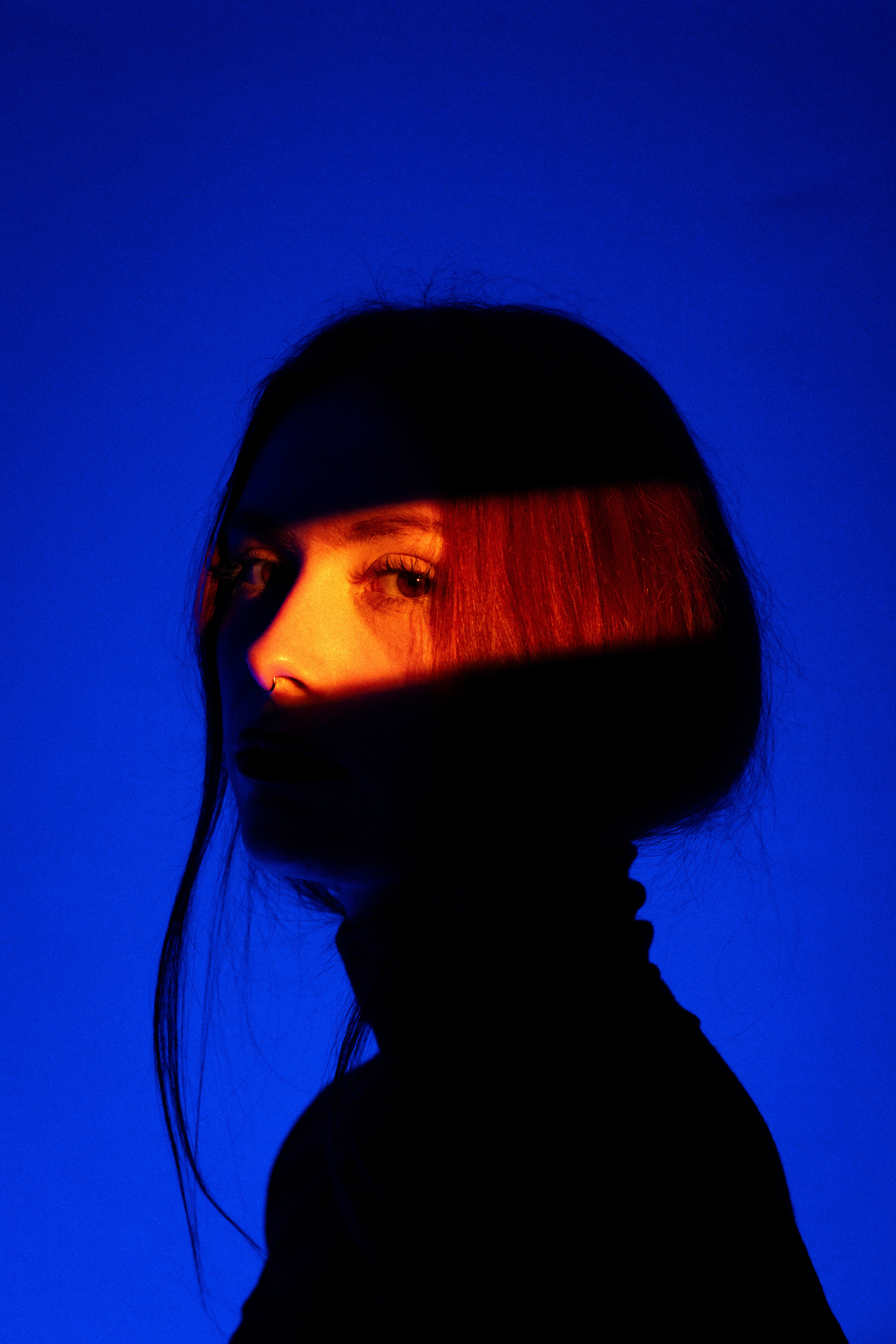 Close-up portrait of a person wearing a gray insulated hooded jacket with the hood up, showing their face framed by the hood against a light background.