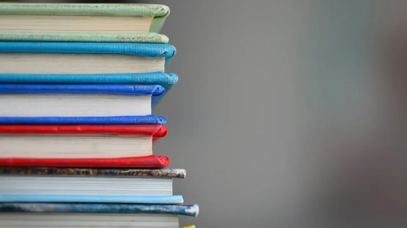 Stack of colourful books on a desk against a grey background — representing reference guides for club sponsorship tax, compliance and documentation (invoices, contracts and reporting).