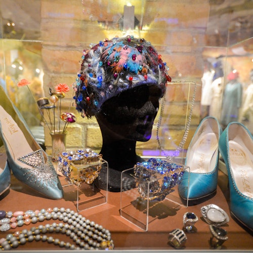 在一个玻璃柜中展示珠饰头饰、绿松石鞋、珍珠项链、手镯和戒指，背景为砖墙。