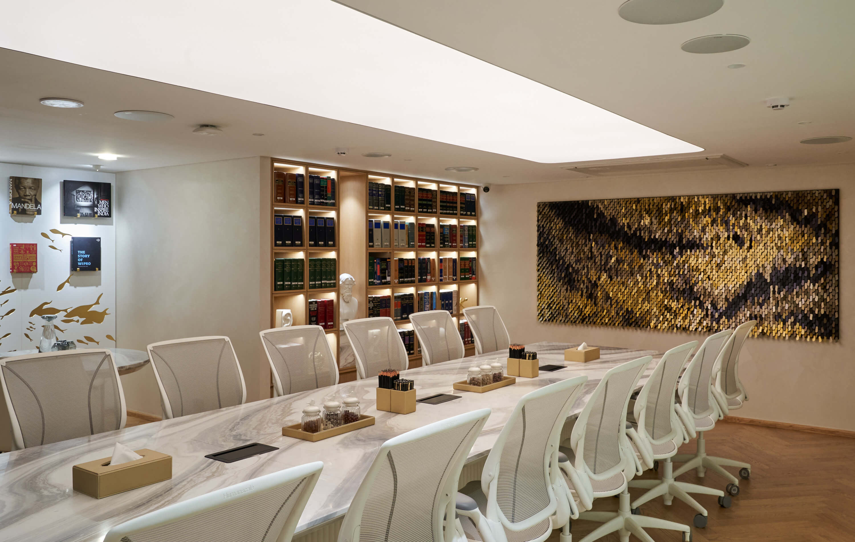 Modern boardroom with marble conference table, white ergonomic chairs, illuminated bookcase, and large textured art wall.