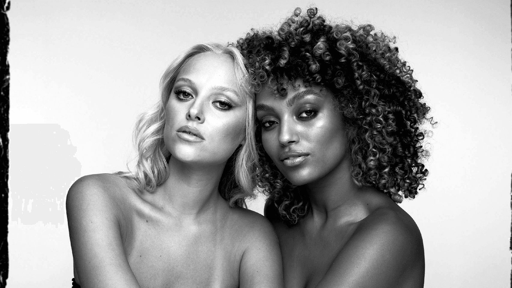 Black and white photo of two femal models looking embraced looking at the screen