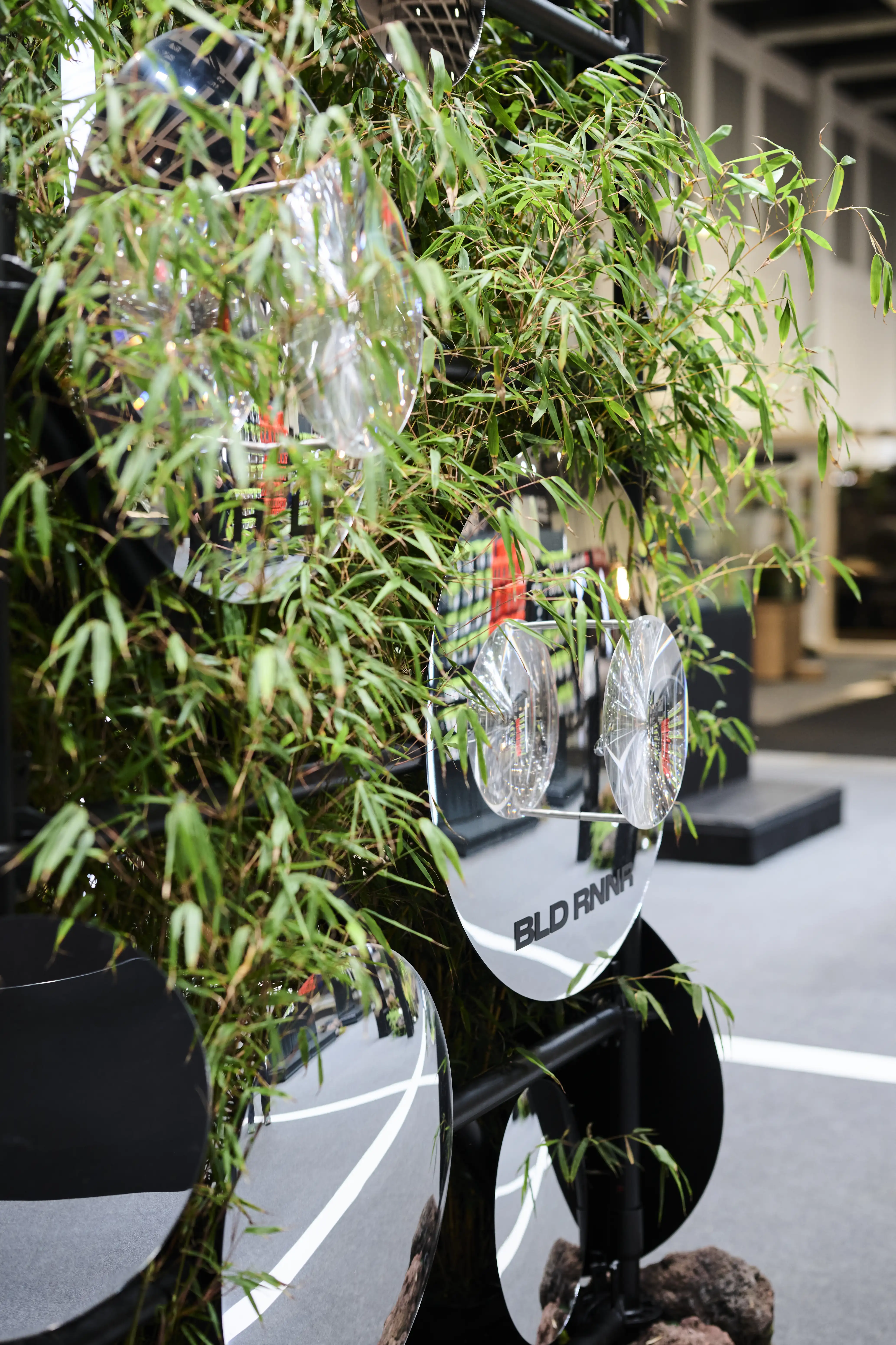 Round mirror discs and bamboo greenery on the black frame installation at the Nays trade fair booth.