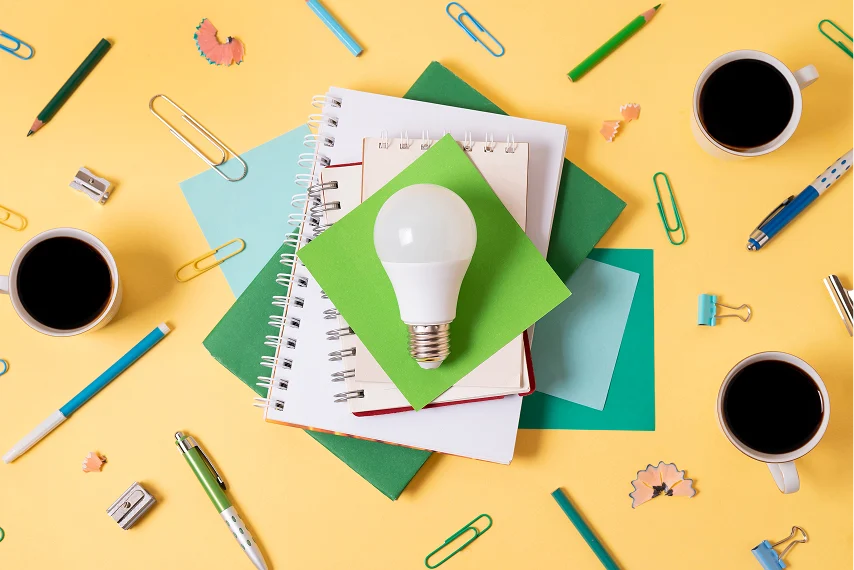 Home office lighting concept with light bulb, notebooks, pens, and coffee symbolizing productivity at work.