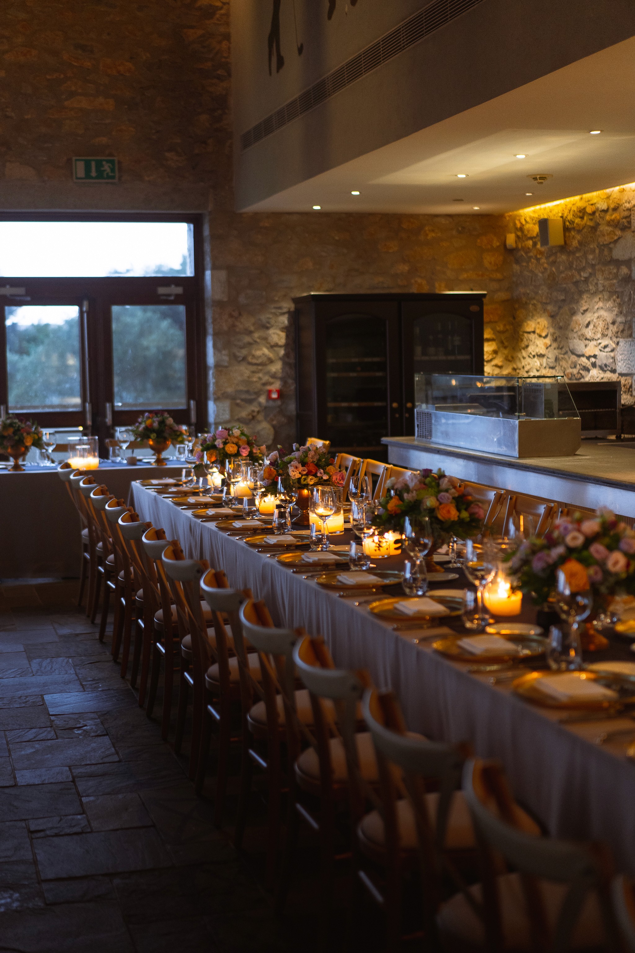 Μακρύ ρουστίκ μοναστηριακό τραπέζι δεξίωσης γάμου με κεριά και ανθοσυνθέσεις