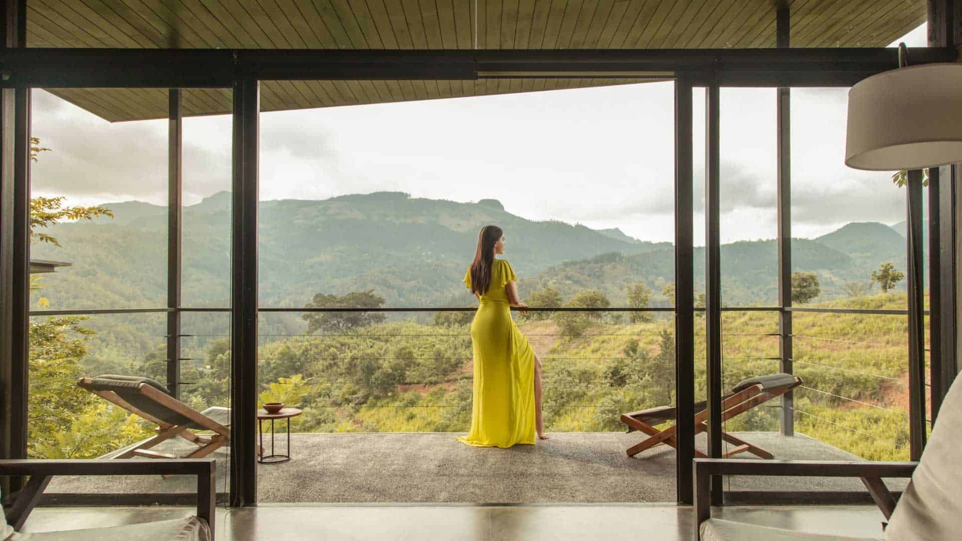 Frau auf Balkon mit Blick auf Berge und Landschaft. Sie trägt ein gelbes Kleid und genießt die Aussicht.