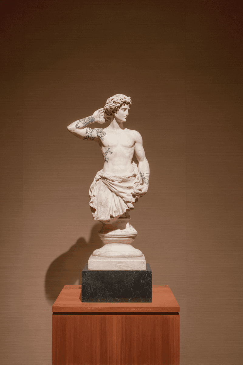 A white marble statue of a woman in a dynamic pose, displayed on a pedestal against a brown wall.