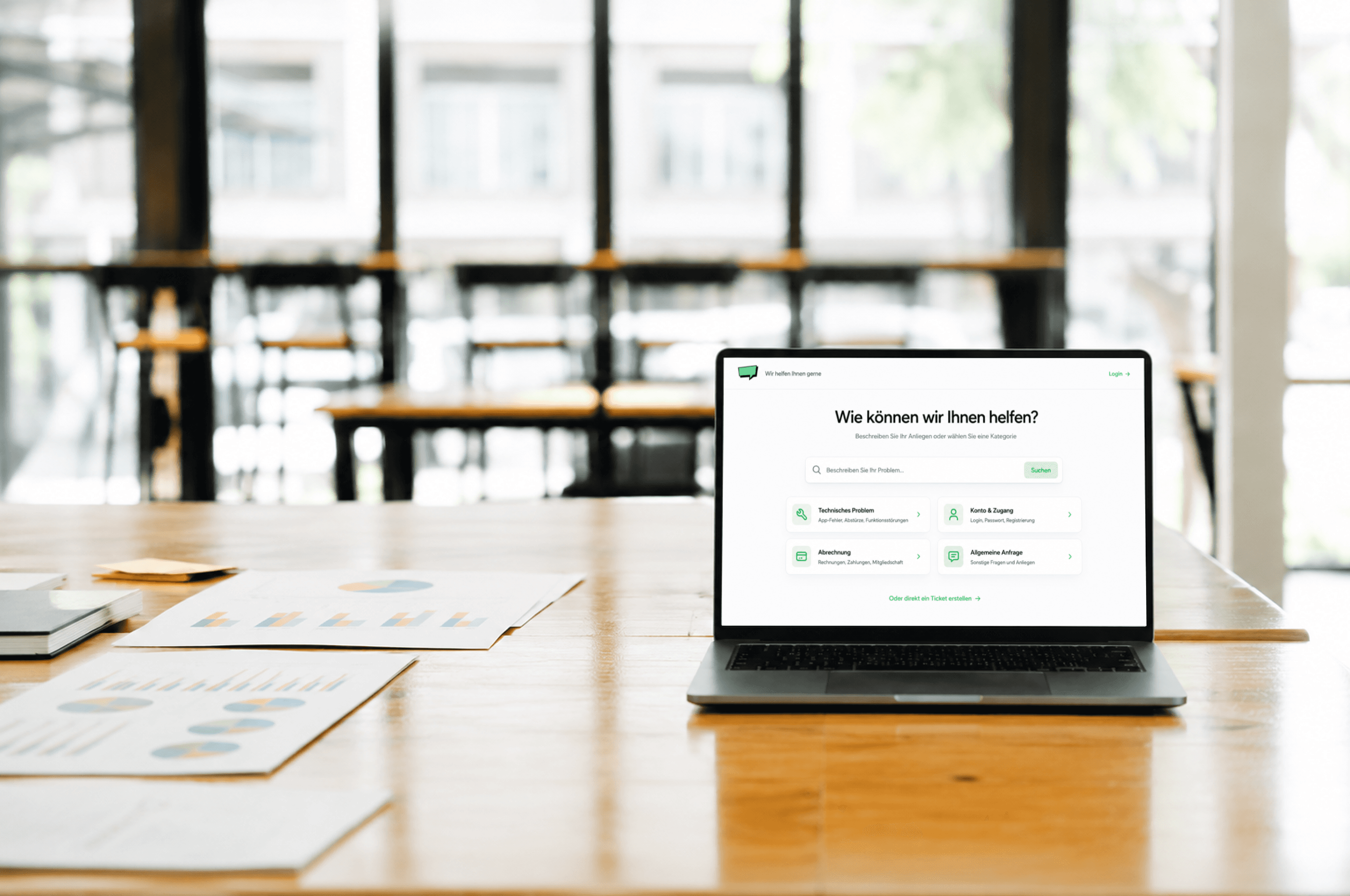 Ein geöffneter Laptop steht auf einem Holztisch neben Dokumenten und zeigt die Startseite eines digitalen Helpdesk-Portals mit Suchfeld und Support-Kategorien.