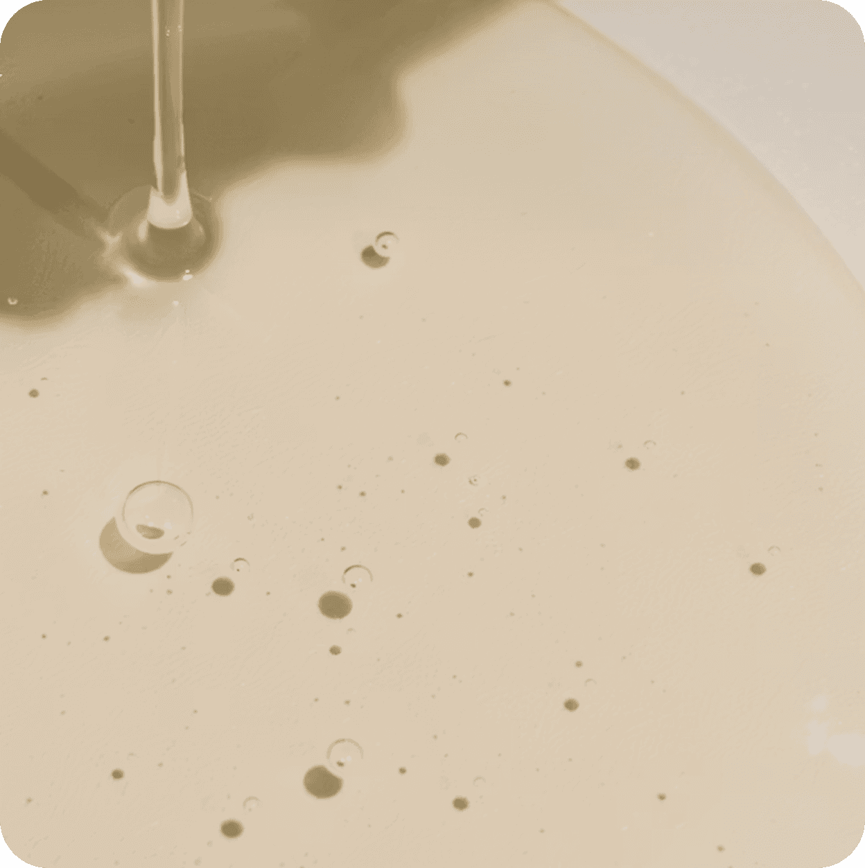 Young woman with a soft smile, resting her chin on her hands, gazing at a small serum bottle on a table