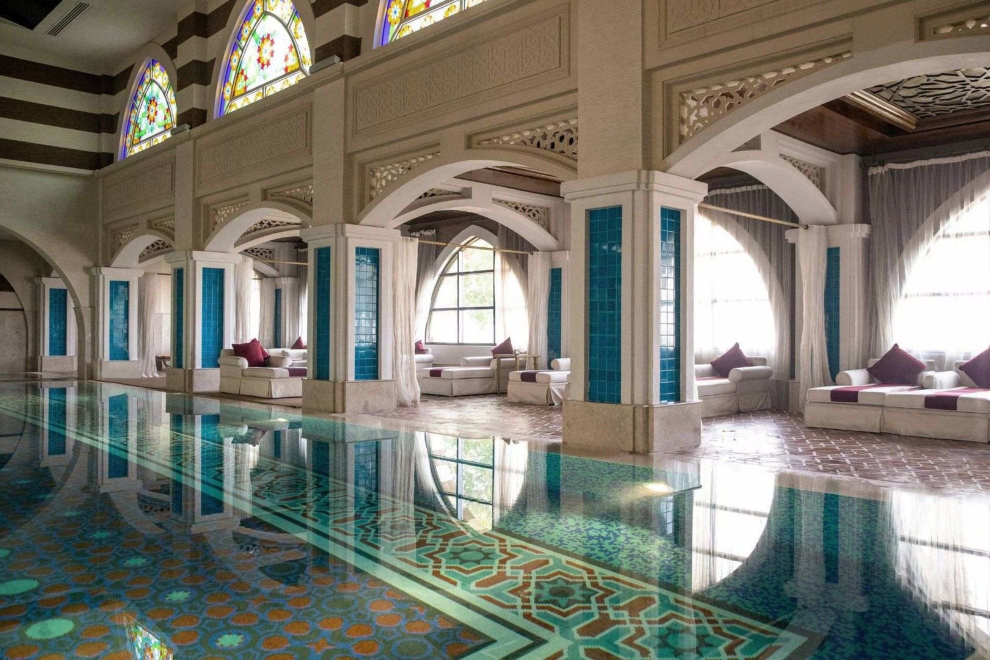 A luxurious indoor space with ornate Middle Eastern architecture, featuring arched columns, tile accents, and stained glass windows.