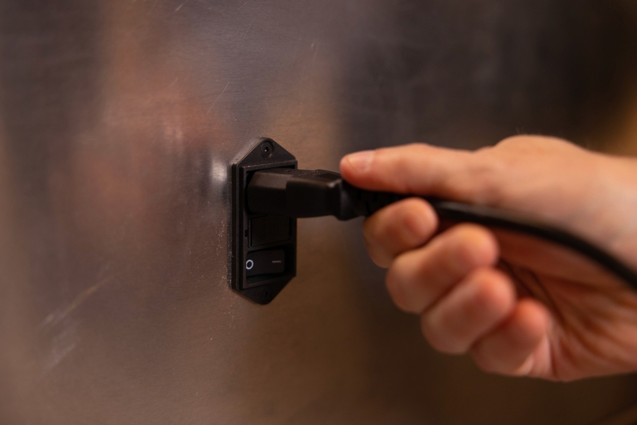 Close-up of a hand plugging the power cord into the BackHug device socket.