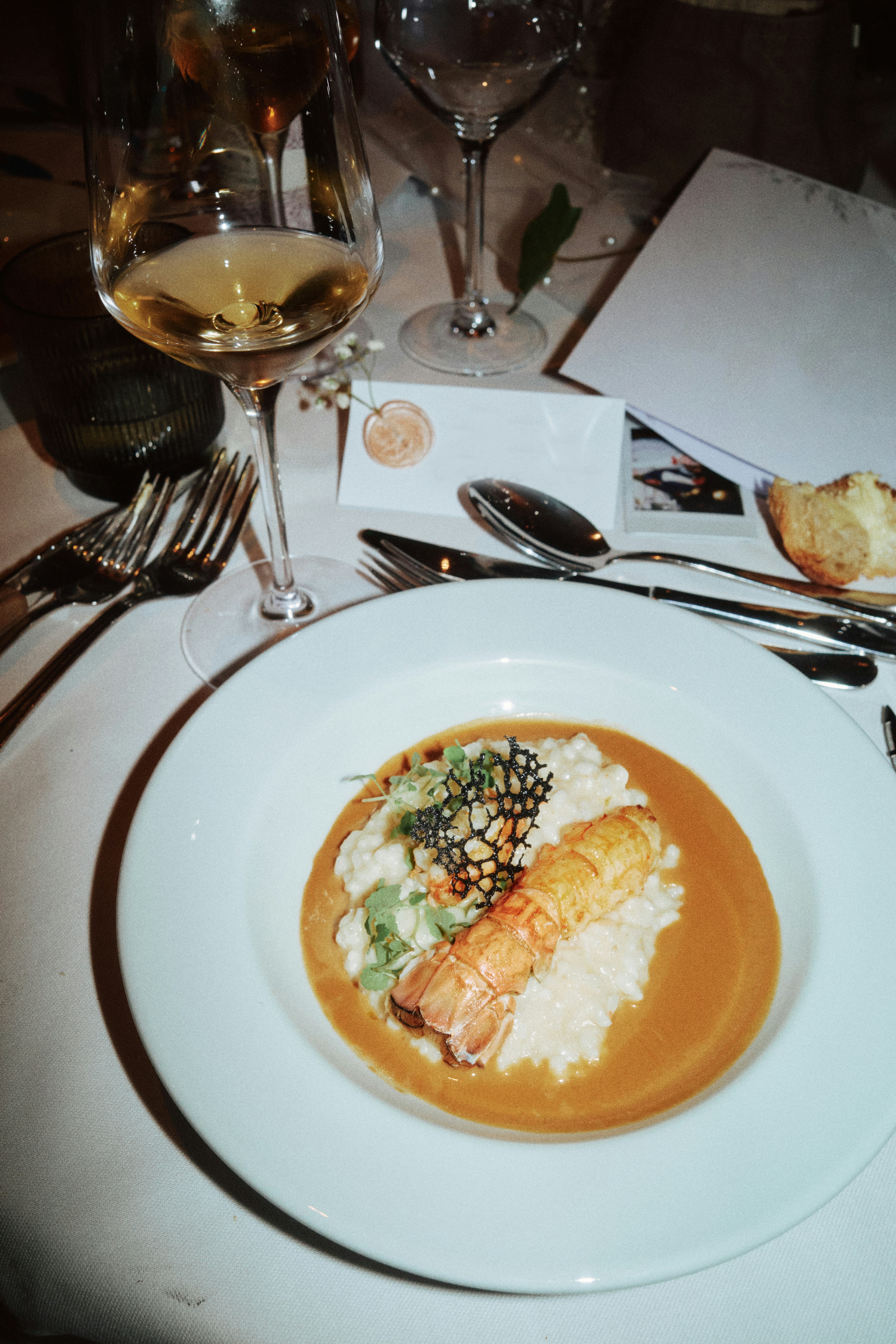 Elegant wedding reception table setting featuring a plated lobster risotto with bisque sauce, white wine glass, silver cutlery, and a wax-sealed place card
