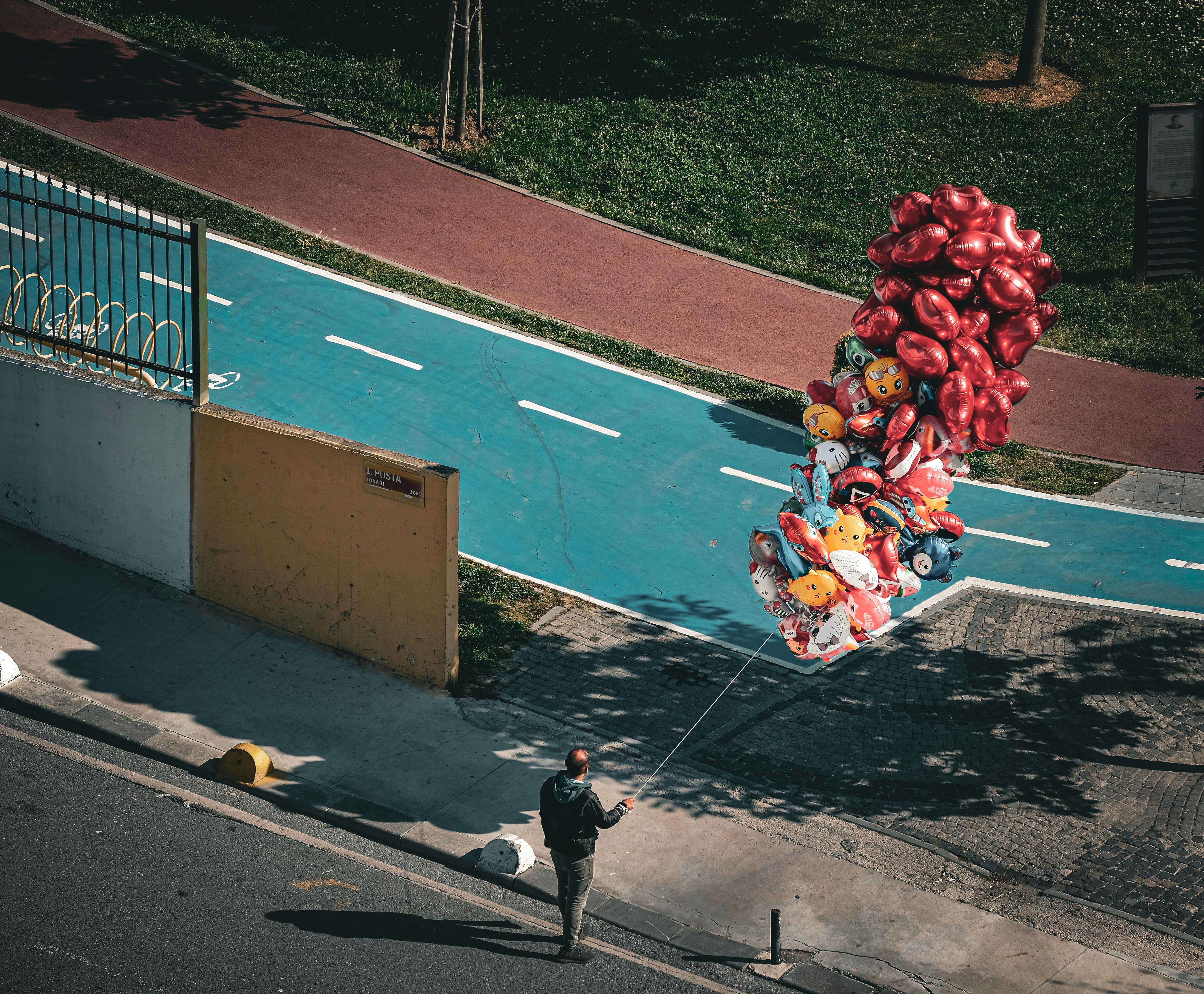 Candid street photography of a person holding a large bunch of colorful balloons in a city.