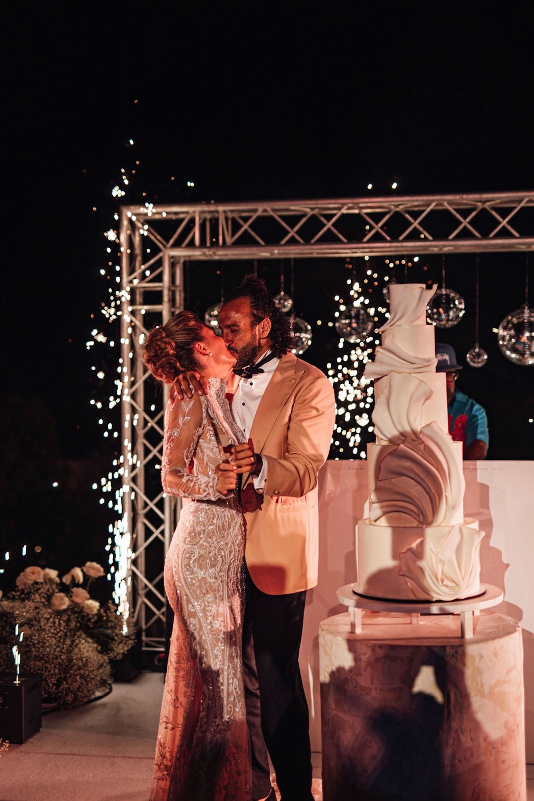 Bride and groom sharing a kiss during nighttime wedding celebration with fireworks in Ibiza.