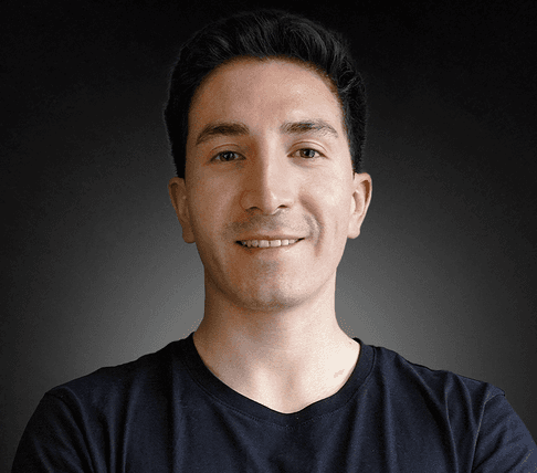 Woman with a short haircut smiling confidently, wearing a blazer and standing in warm natural light with modern architecture behind her.