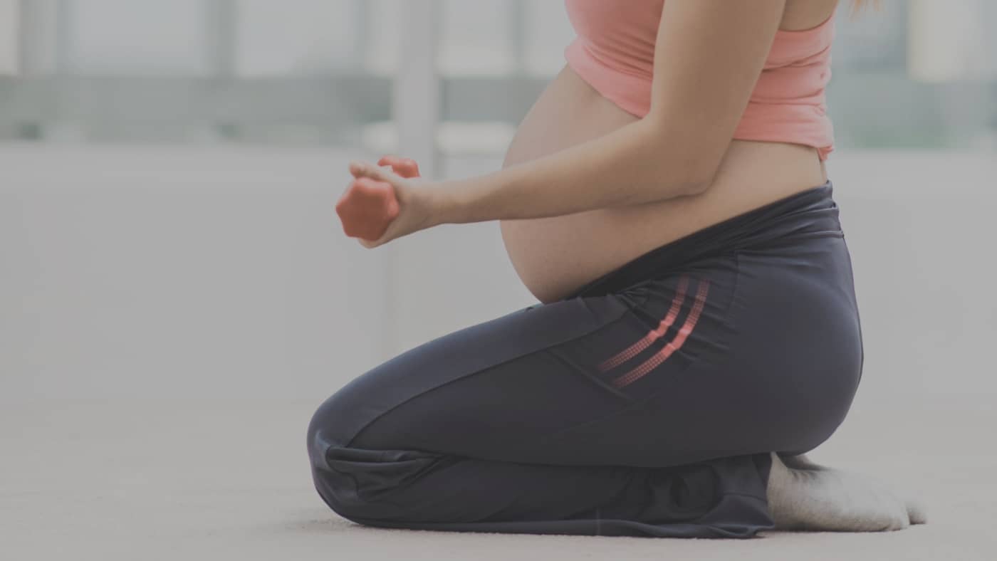 Jeune femme enceinte souriante s'étirant sur un tapis de yoga pendant son deuxième trimestre de grossesse, dans un salon lumineux, avec une haltère à la main.