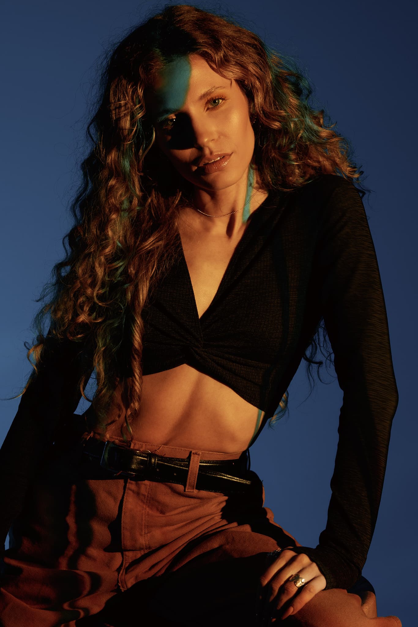 A model sits with confidence against a dark blue backdrop, lit with creative studio lighting in Shreveport.