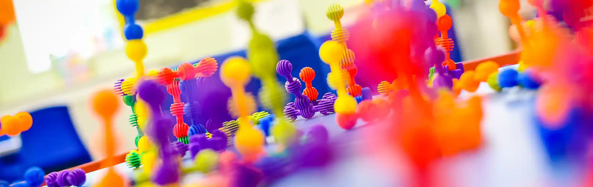 Close-up of colorful, blob-like, bouncy balls on thin strands, resembling molecular structures or whimsical art.