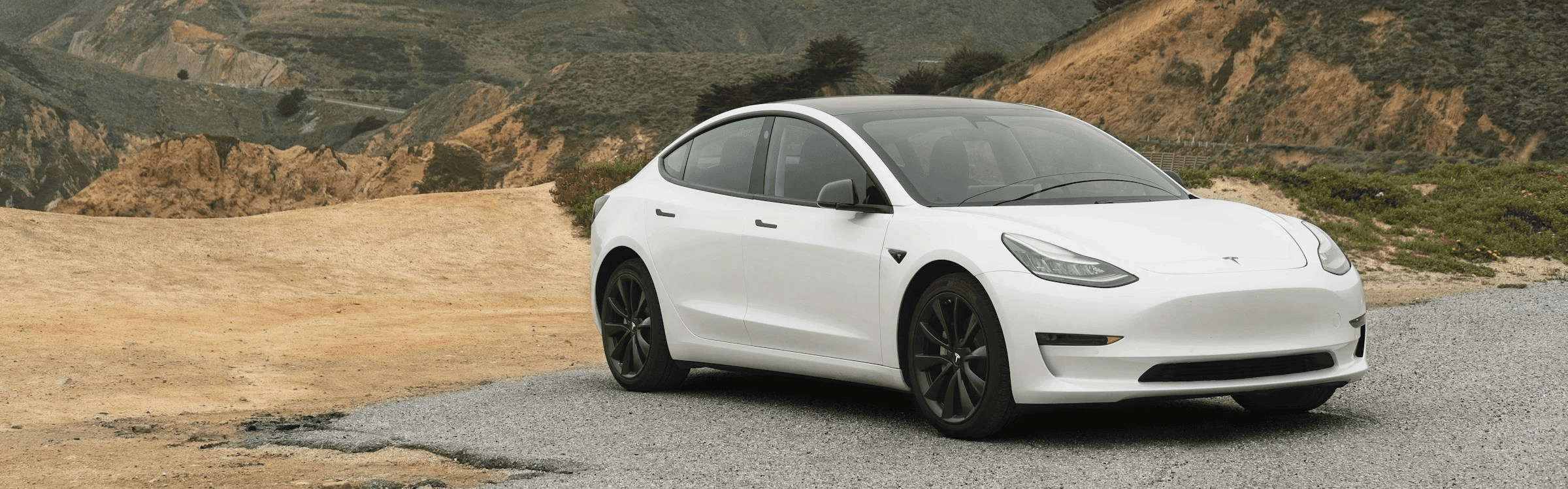 Tesla Model 3 blanche dans un décor naturel montagneux, berline électrique vue de face en stationnement