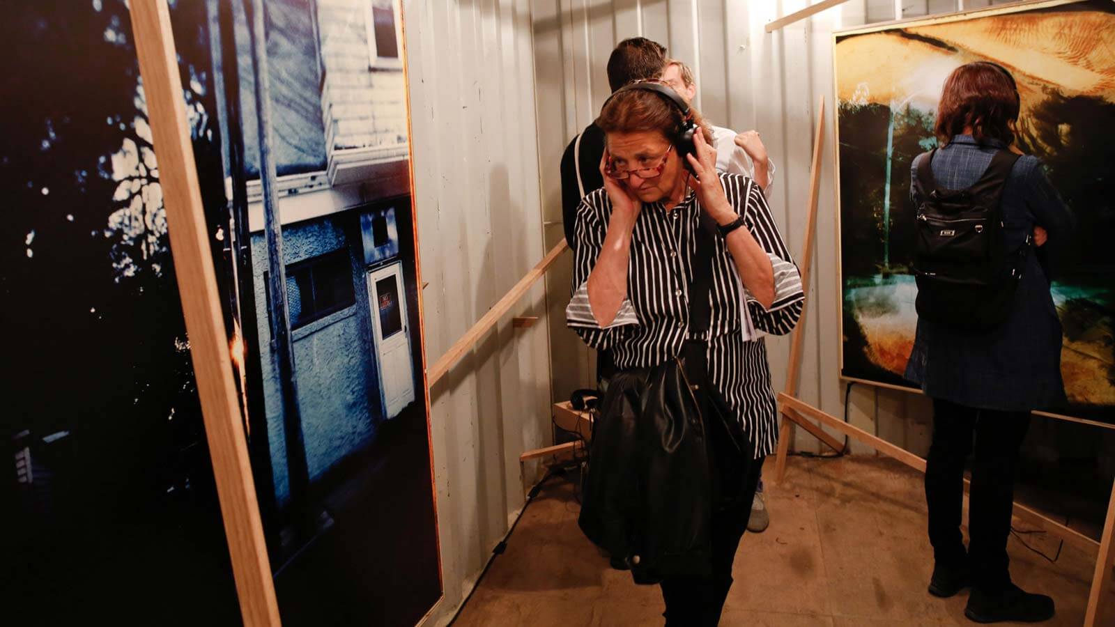 Person wearing headphones and striped shirt in an art installation with large photographs mounted on white walls in a container space
