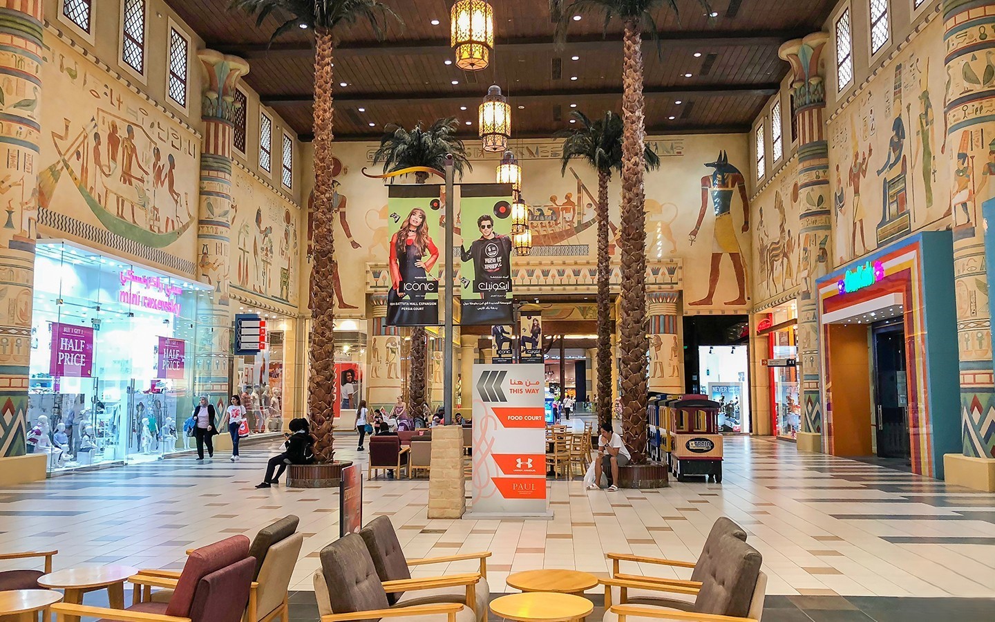 Interior of a shopping mall with high ceilings, columns resembling palm trees, and walls decorated with Ancient Egyptian murals.