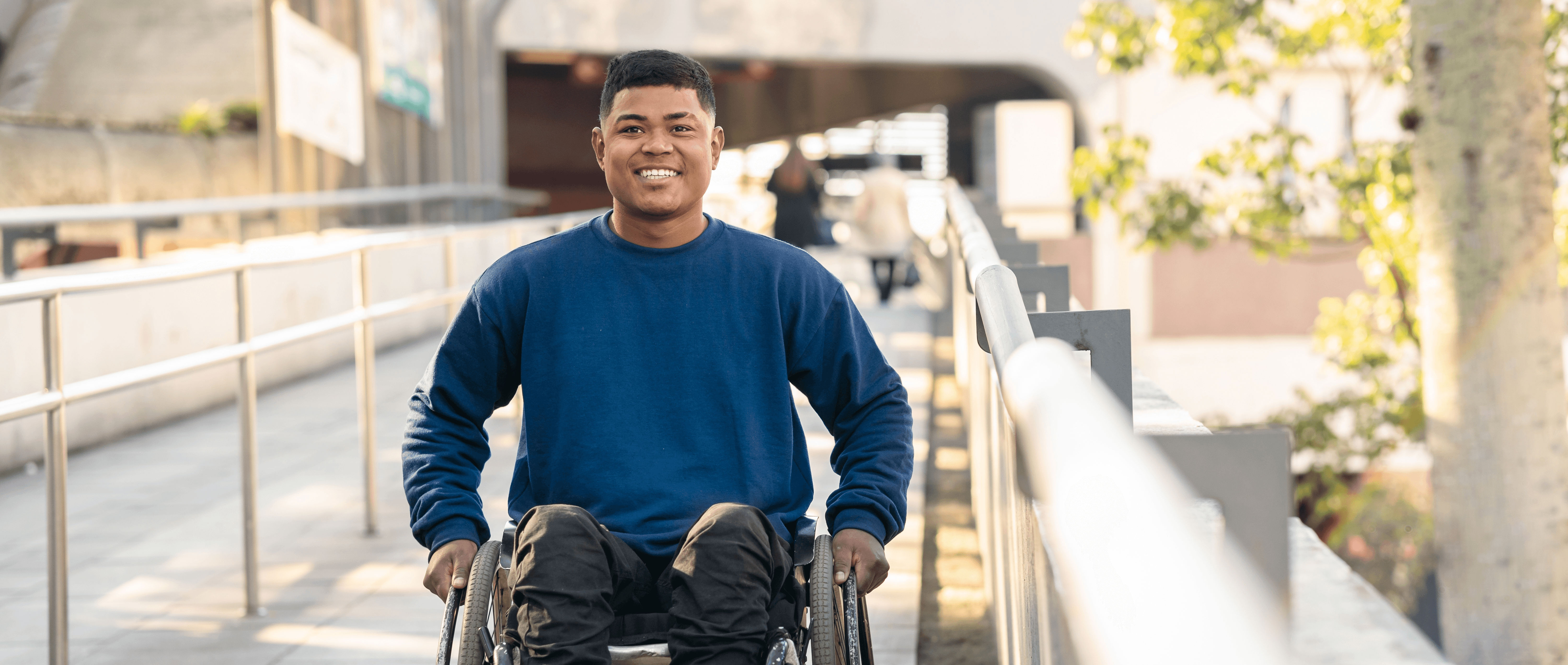 A wheelchair user smiling on an outdoor ramp.