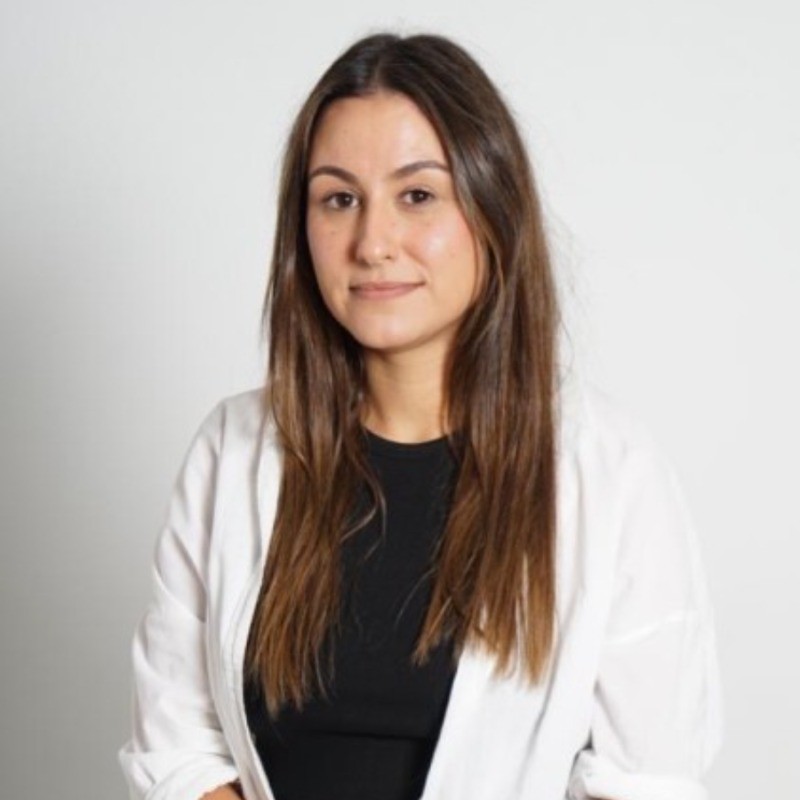 Woman with long brown hair, wearing a white shirt and black top