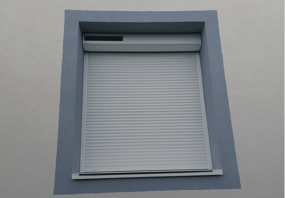 Fenêtre avec volet roulant blanc fermé, encadrement bleu sur façade blanche