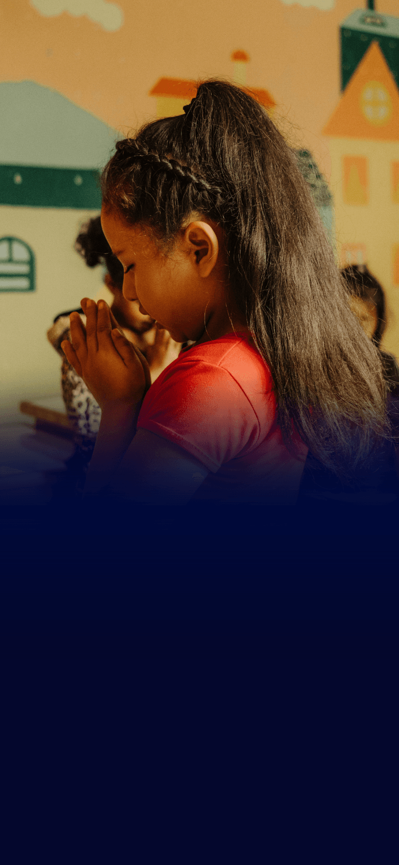 a young girl sitting at a desk with her hands clasped