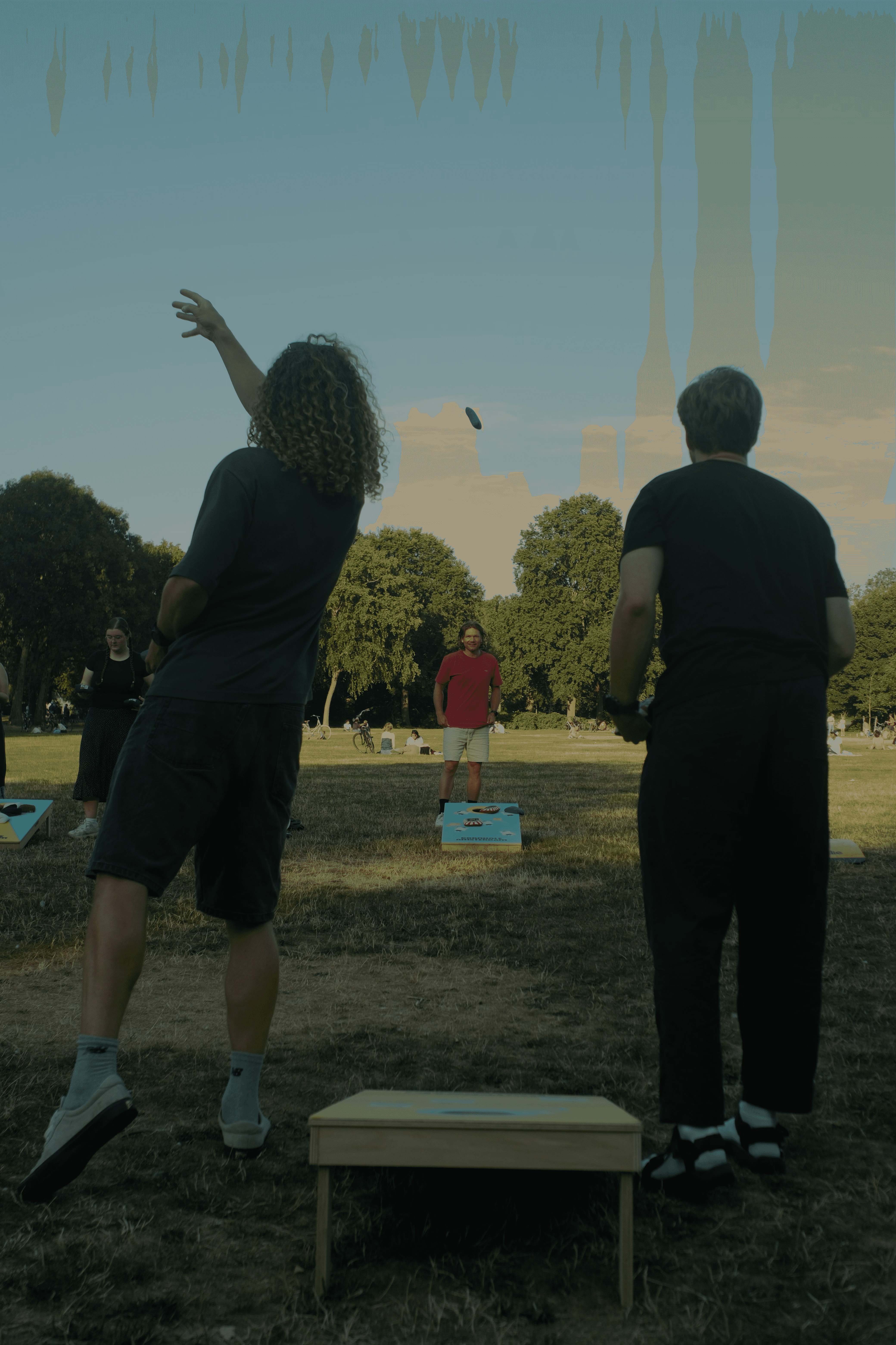 People enjoying a sunny day in an Amsterdam park during a cornhole session