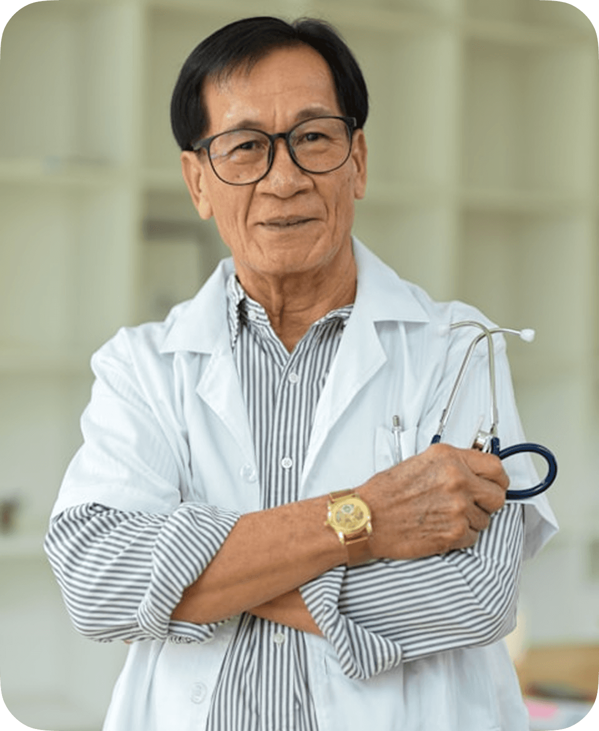 An elderly man in a white doctor's coat, wearing glasses and a gold watch, stands confidently holding a stethoscope in a bright, modern office setting.