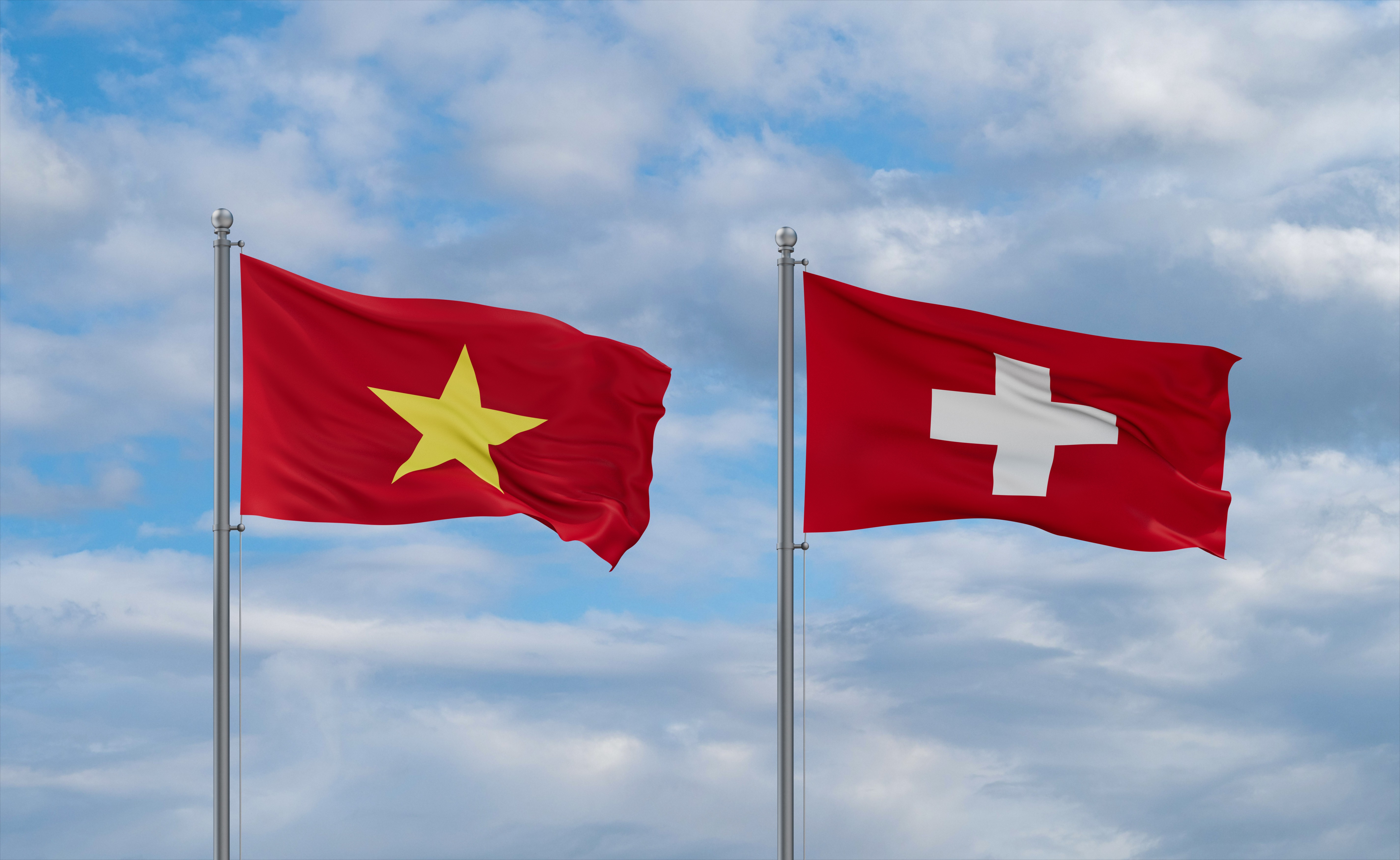 Vietnamese and Swiss flags flying side by side against a cloudy blue sky.