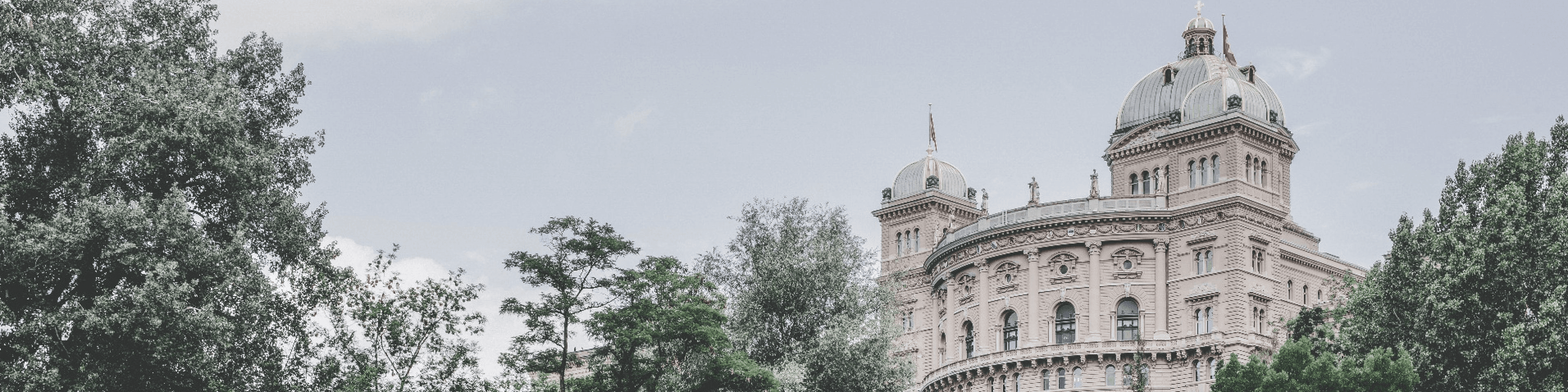 Swiss Federal Palace surrounded by trees, representing the role of government in shaping policies and legislation for sustainable mobility and electromobility initiatives in Switzerland