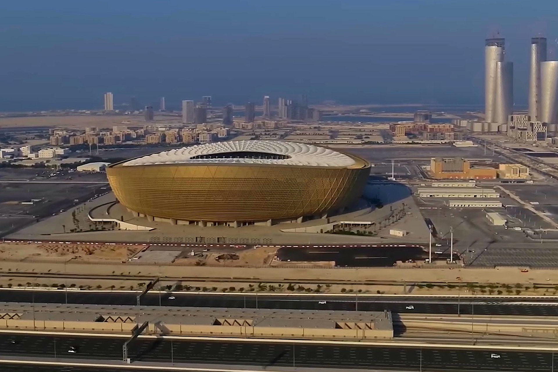 Le stade de Lusail vu du ciel, un bol doré posé au nord de Doha, avec les tours de Lusail derrière