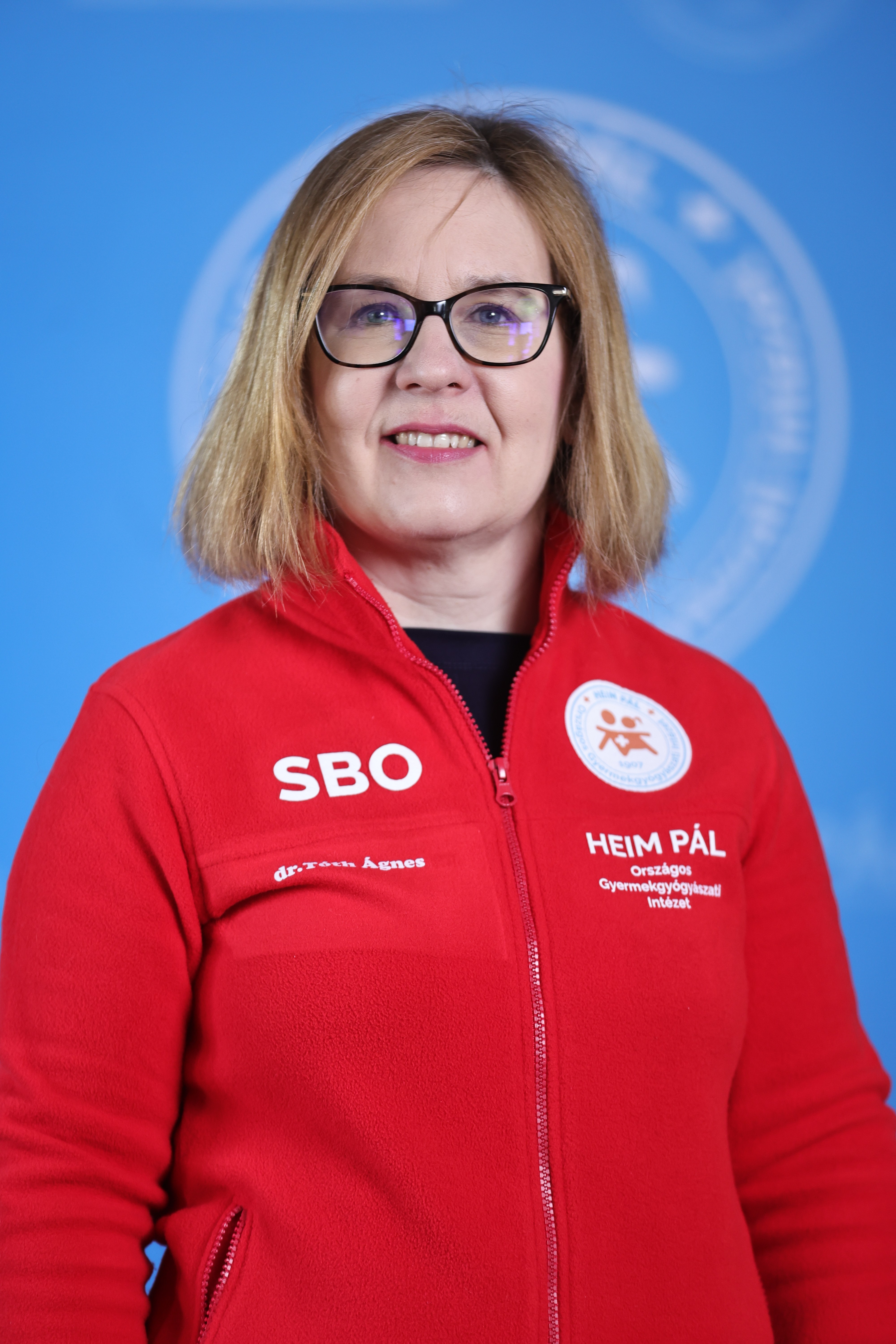 Szőke szemüveges nő piros kardigánban