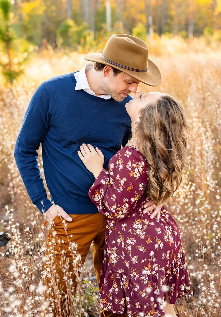 Couple in a cowboy hat and floral dress kissing in a golden field, by Sioux Falls, SD couples photographer Kelsey Lynn