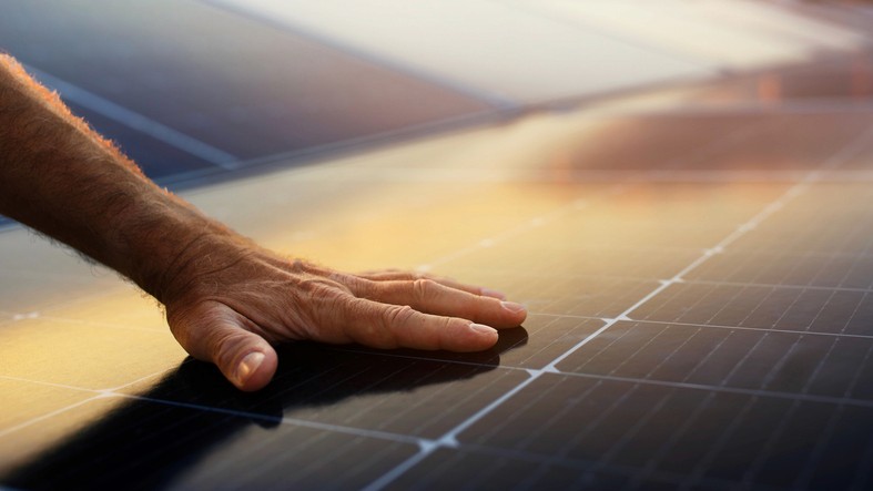 Eine Hand berührt sanft eine glatte Oberfläche vor dem Hintergrund eines farbenfrohen Sonnenuntergangshimmels.