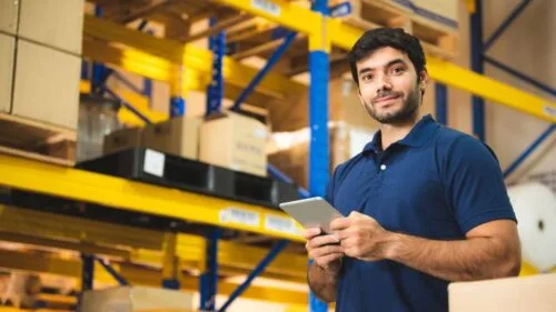 Warehouse worker holding a tablet in front of shelves with stacked boxes