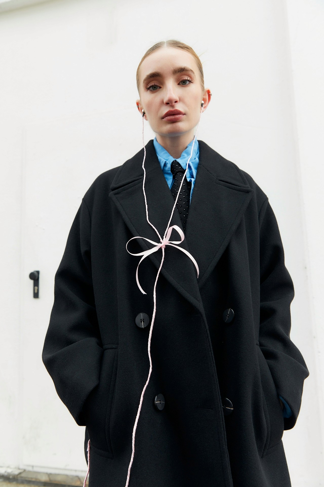 A woman standing, wearing a stylish, long black coat.