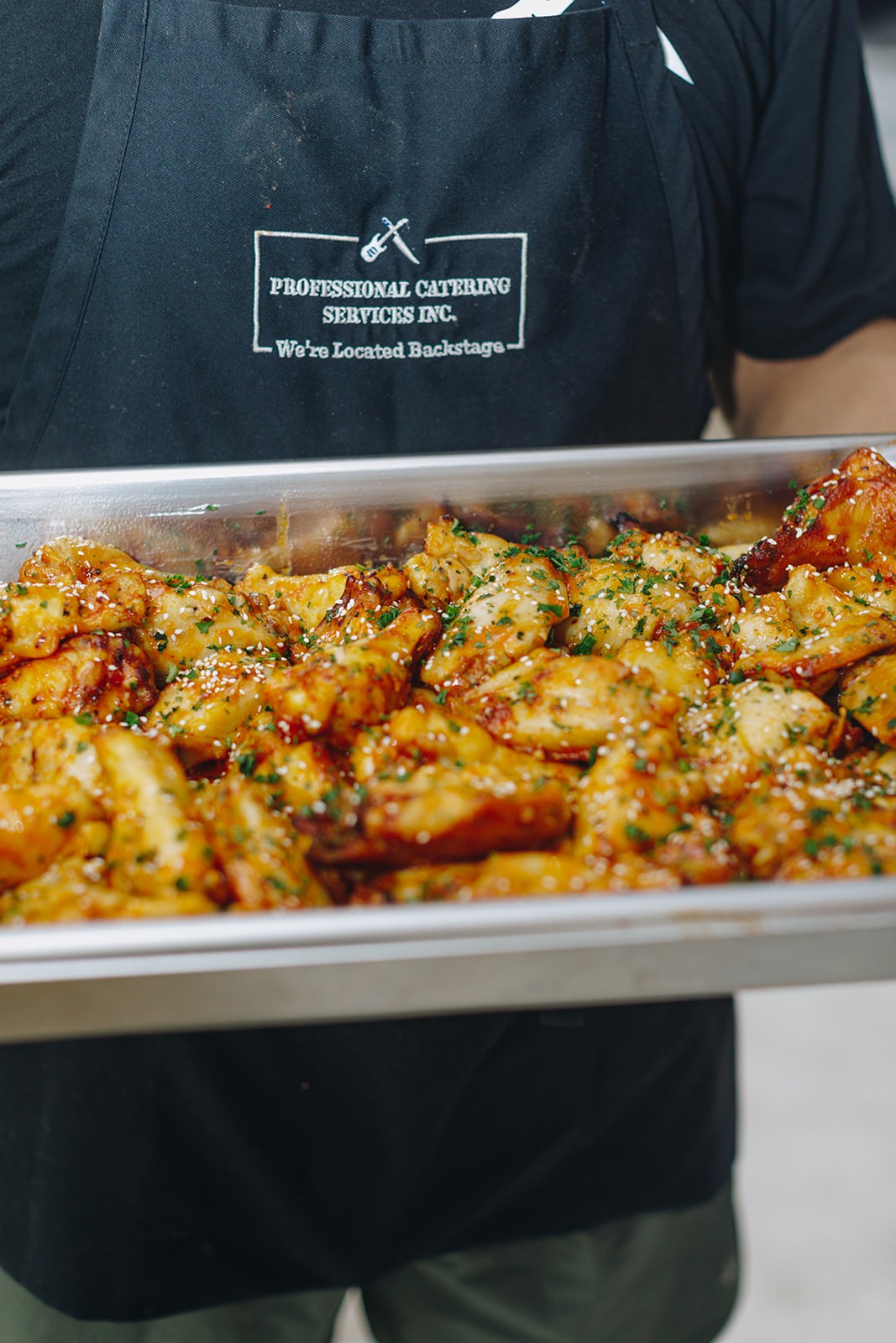 A person holding a tray filled with golden-brown, crispy snacks or appetizers in a kitchen setting.