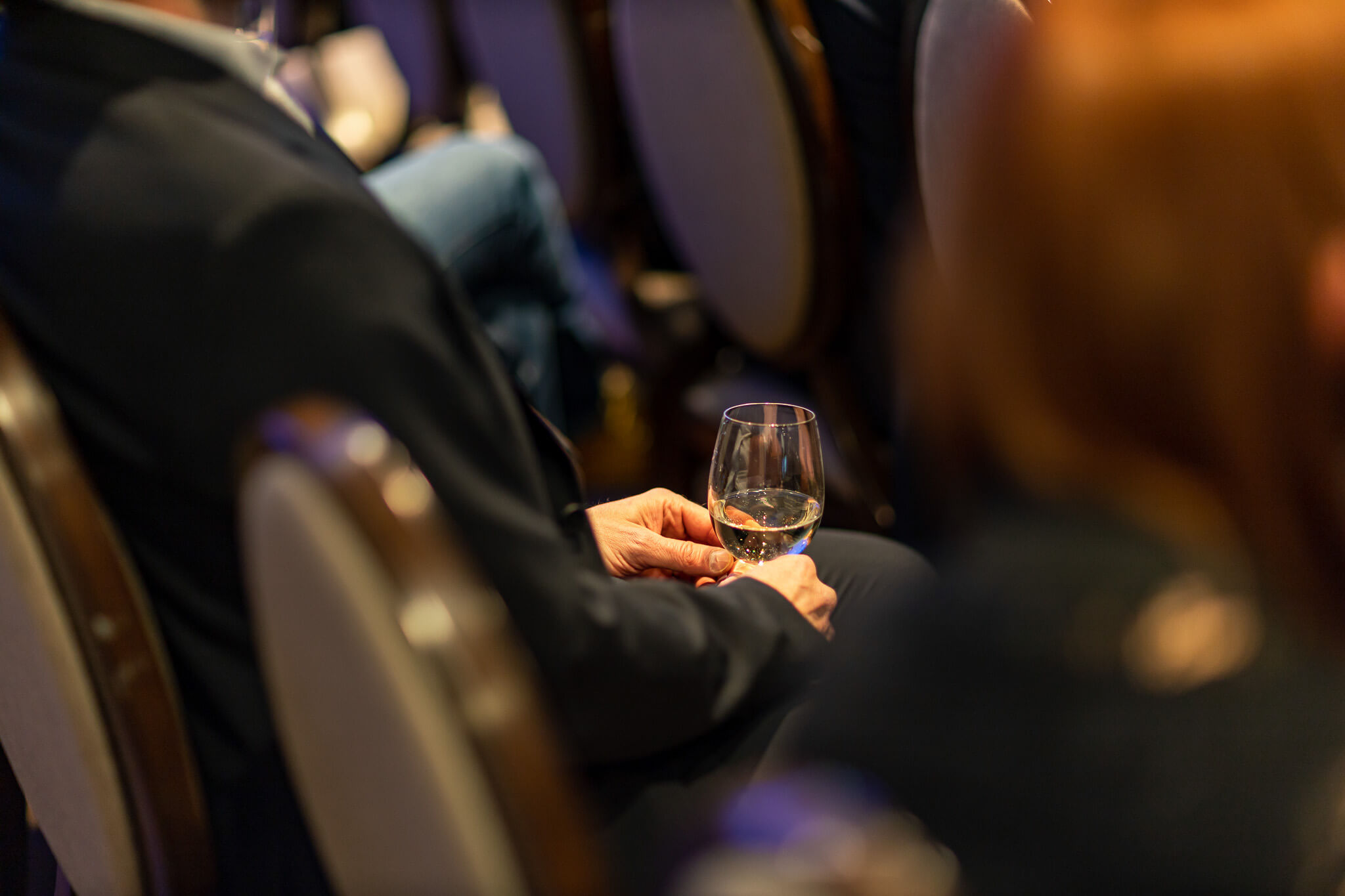 Person holding a glass of wine while listening during a professional networking event
