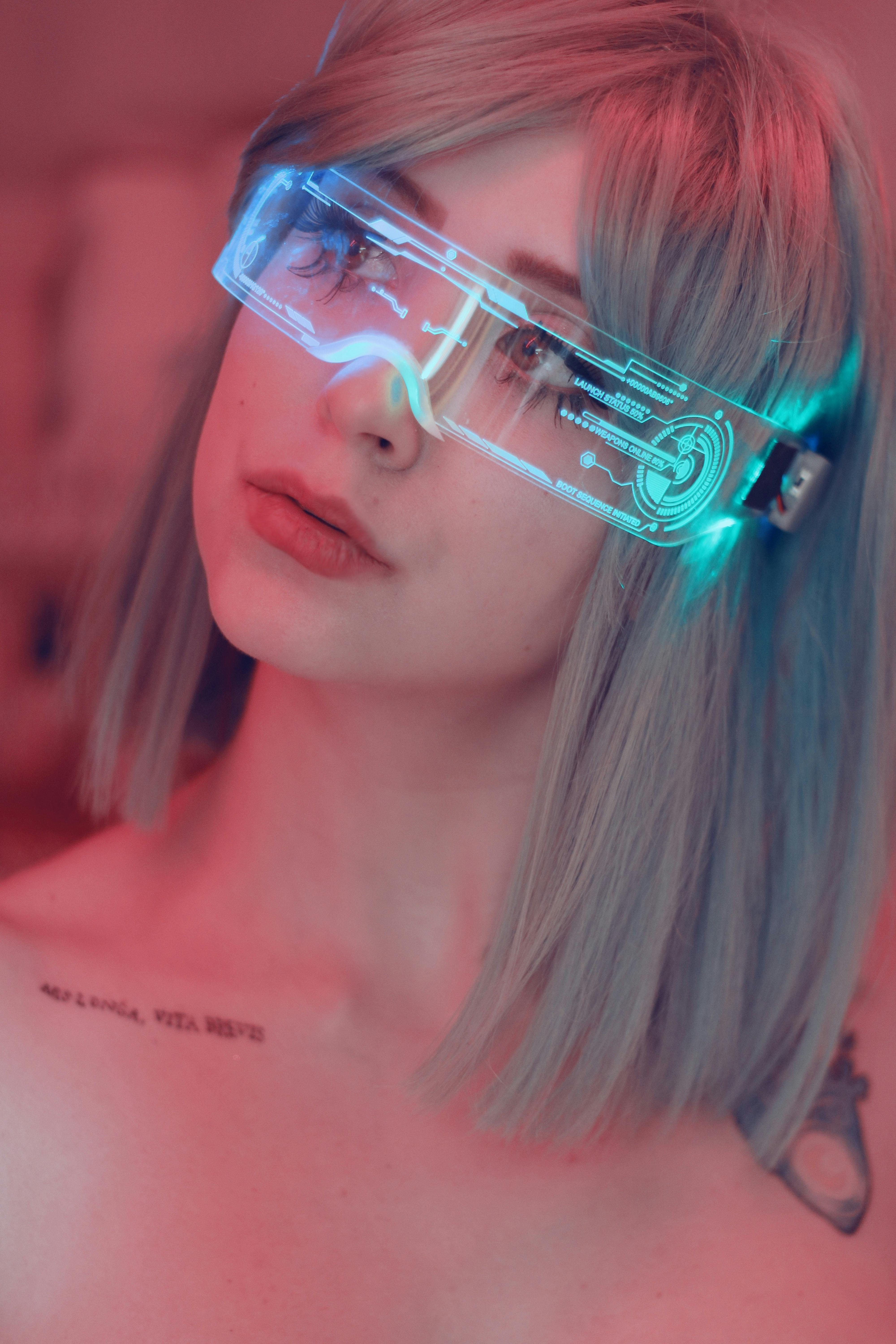 A young person with short, silver hair wears colorful, glowing glasses against a softly lit background.