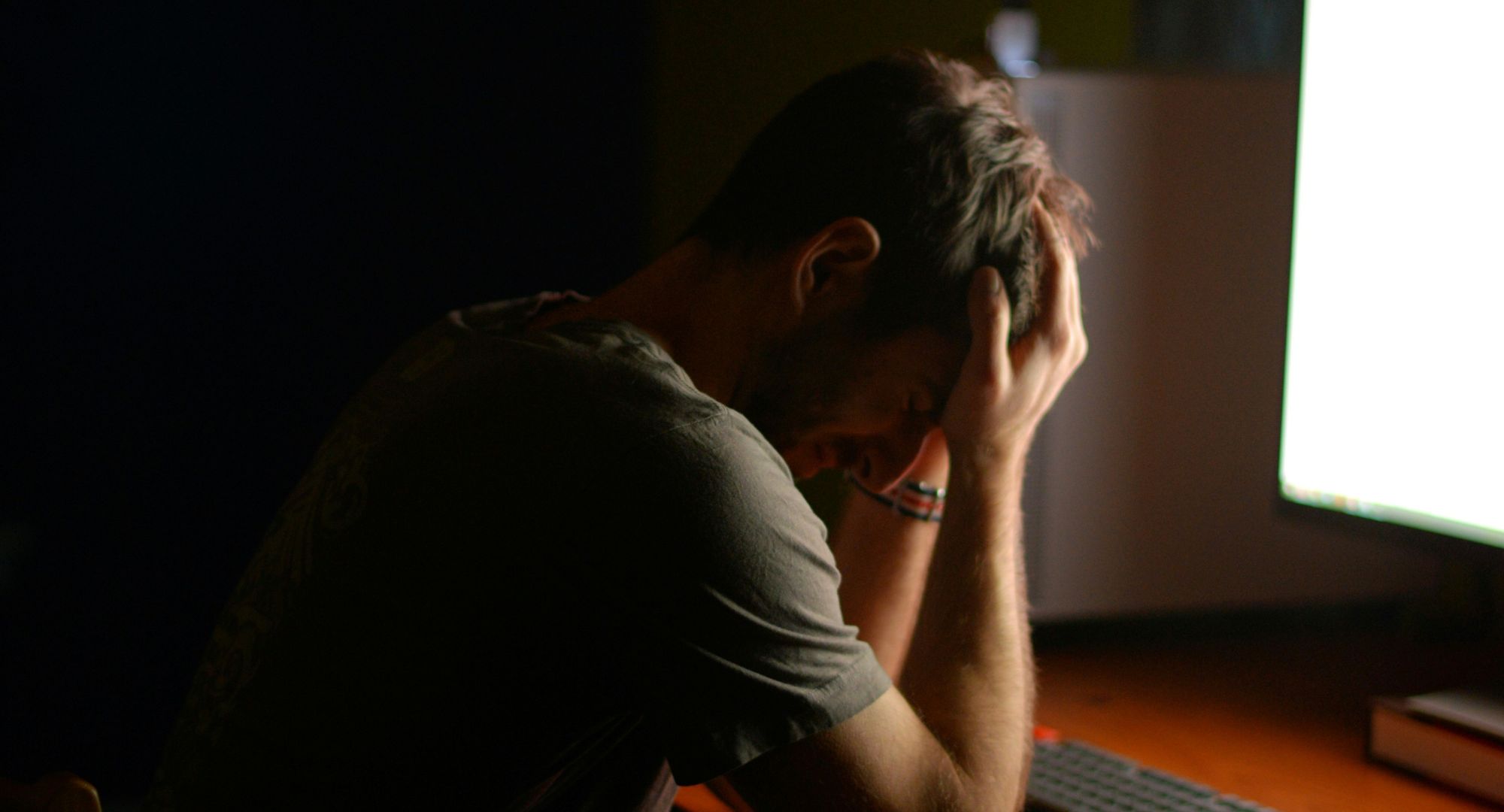 homem sentado em frente à mesa com um computador com o semblante preocupado, de cabeça baixa