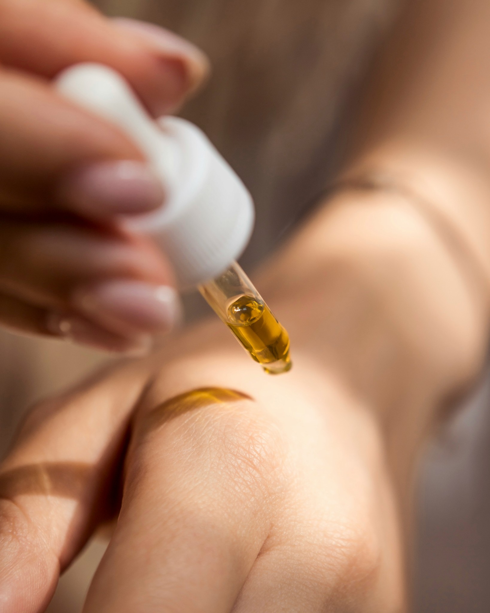 A close up of someone applying a droplet of serum to the top of their hand