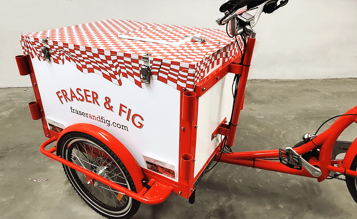 a red-and-white bicycle with fridge box attachment and vinyl wrap on top, reading Fig & Fraser on the sides and front