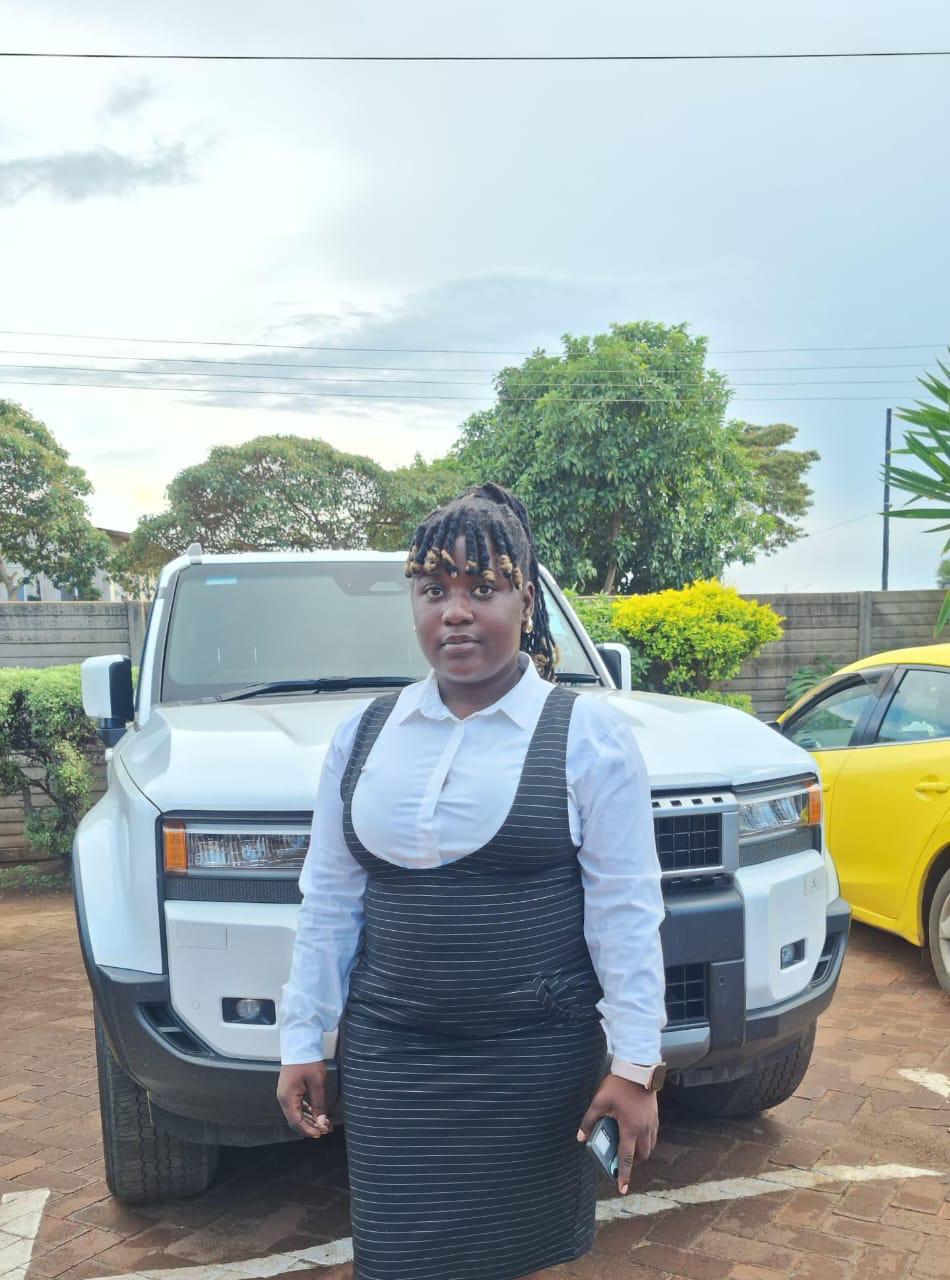 Smiling young woman with curly hair sitting at a laptop, in front of a teal wall.