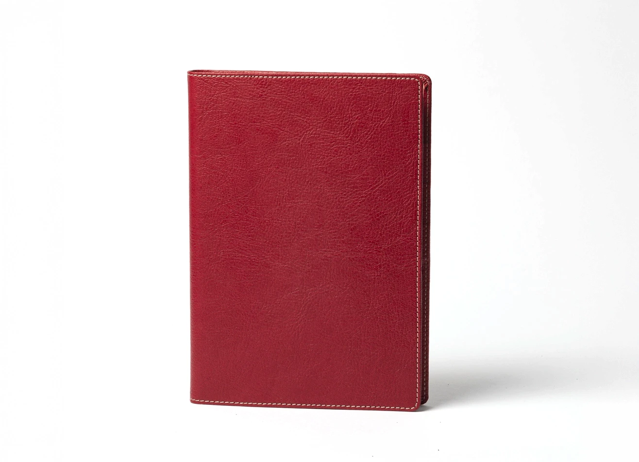 Front view of standing red textured notebook with white stitching.