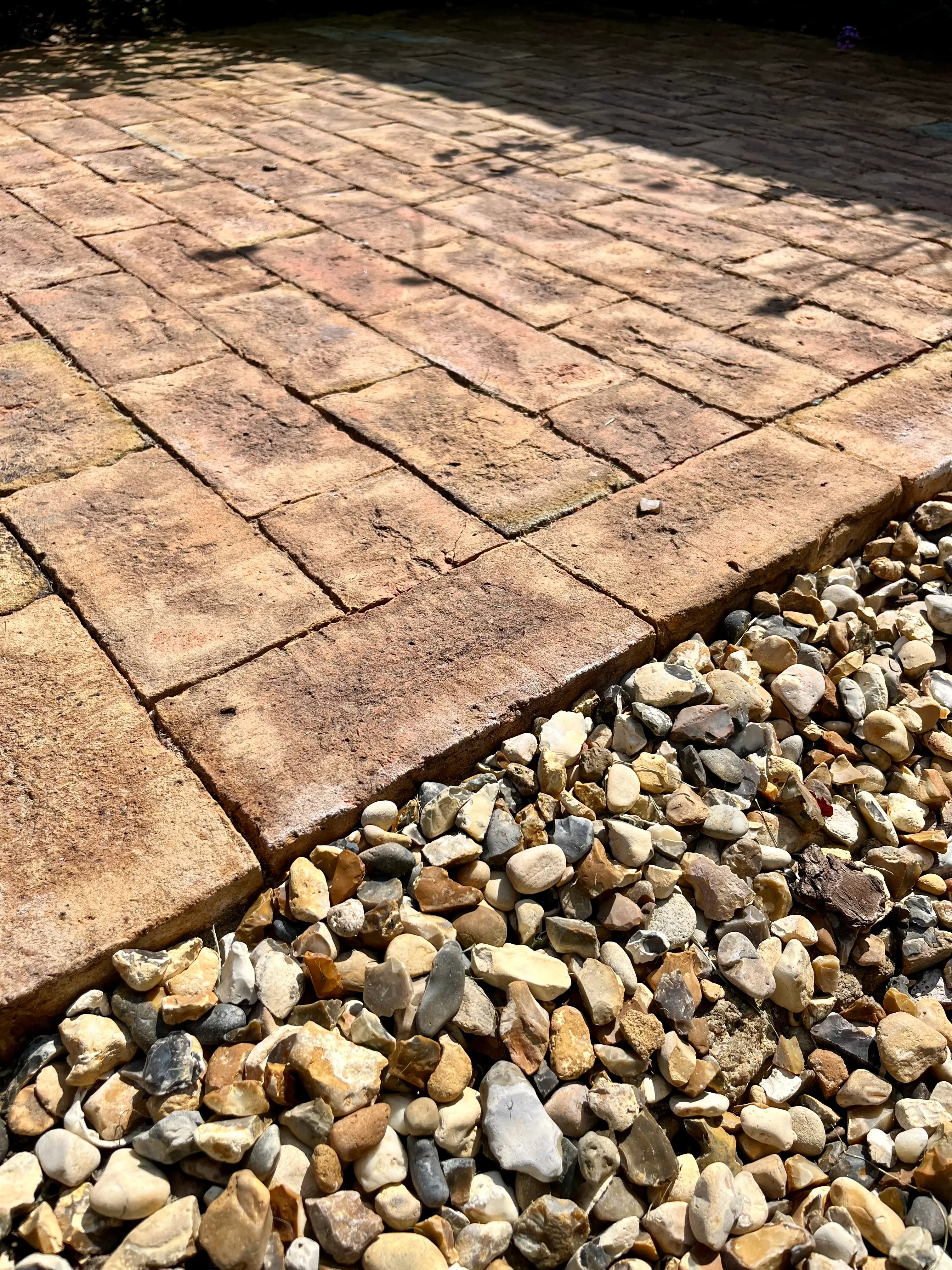 Close-up of a textured stone pathway next to a bed of small gravel stones, with sunlight casting shadows.