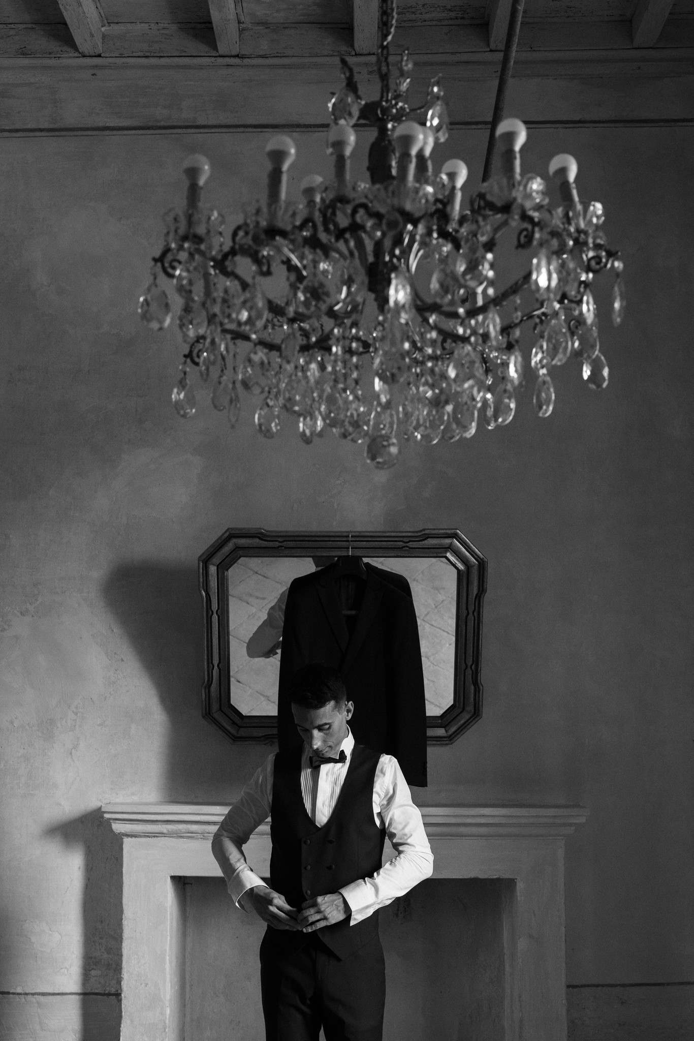 Sposo in gilet nero e farfallino riflesso nello specchio sotto lampadario di cristallo, Villa Ferrari