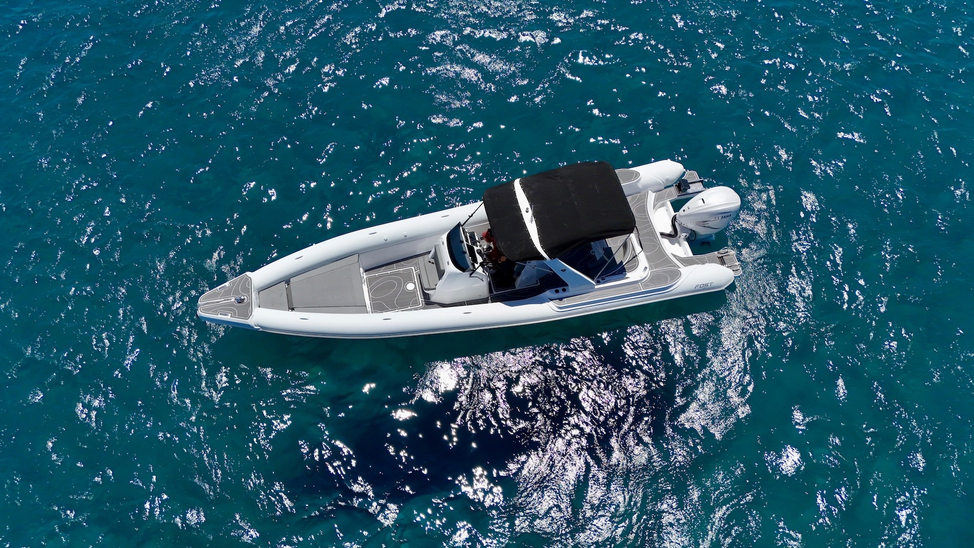 Aerial view of white Fost Matrix 32 with black bimini top floating on crystal clear turquoise waters.