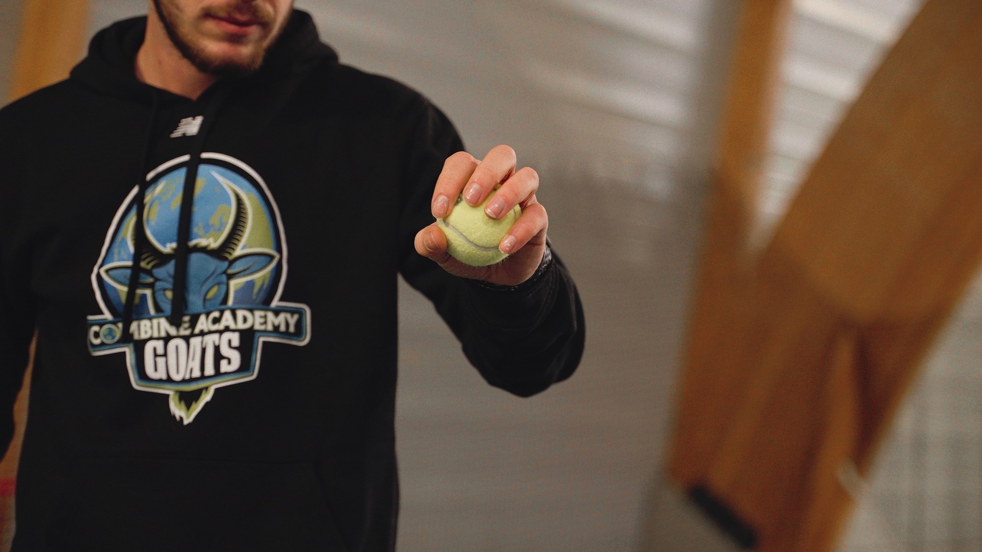 Gros plan sur une main tenant une balle de tennis, sweat Combine Academy GOATS.